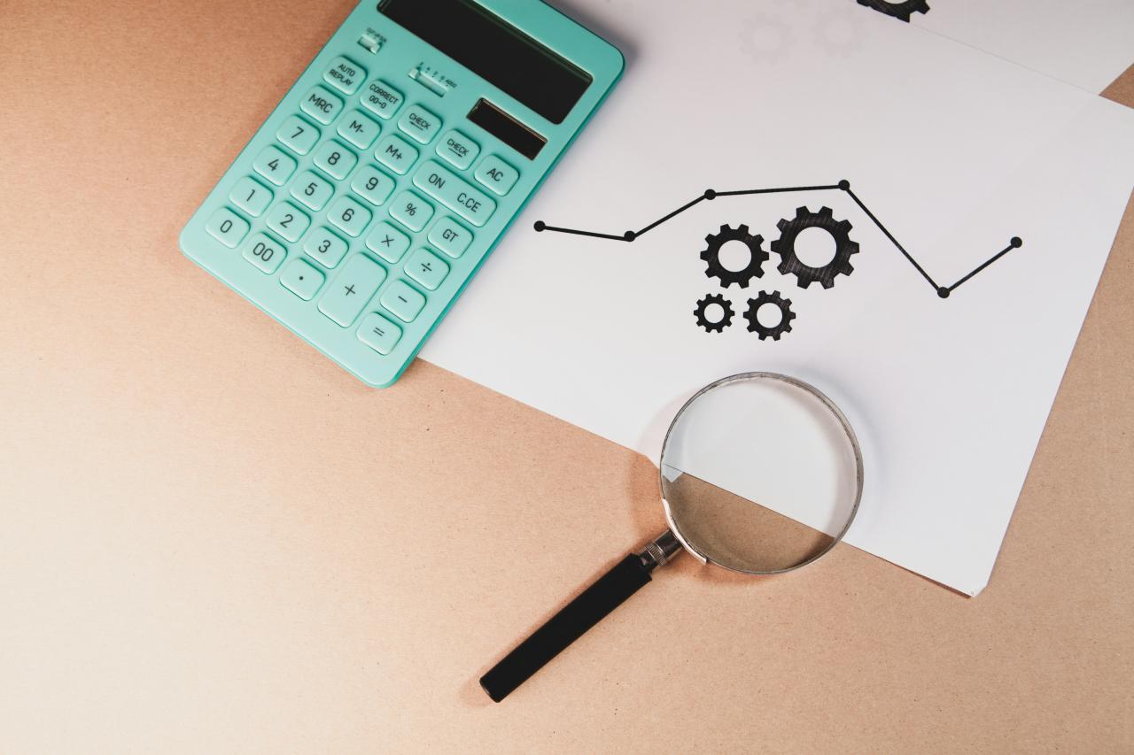 Calculator, magnifying glass, and chart with gears on paper.